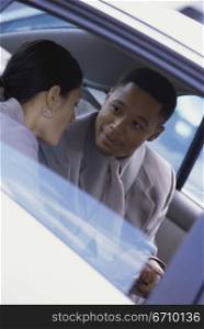 Businessman and a businesswoman talking to each other in the back seat of car
