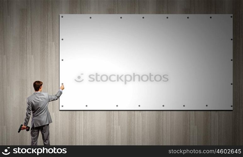 Businessman and banner on wall. Rear view of businessman fixing white blank banner with drill
