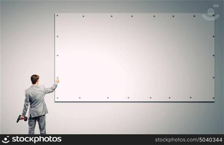 Businessman and banner on wall. Rear view of businessman fixing white blank banner with drill