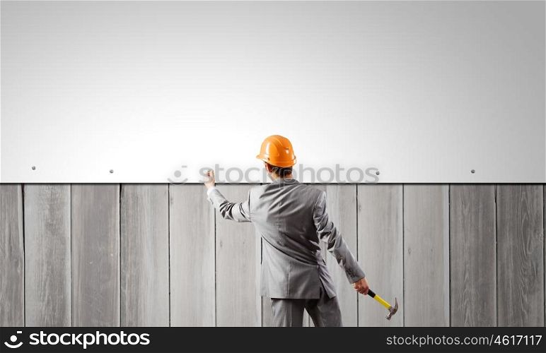Businessman and banner on wall. Rear view of businessman fixing white blank banner with hammer