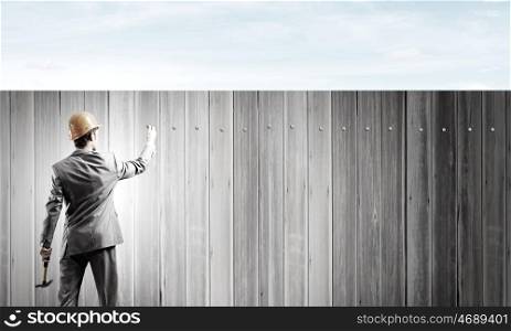 Businessman and banner on wall. Rear view of businessman fixing white blank banner with hammer