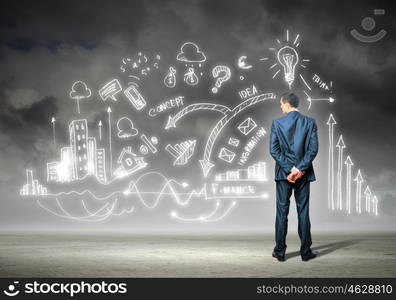 Businessman and business sketch. Back view image of young businessman standing against business sketch