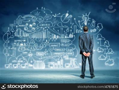 Businessman and business sketch. Back view image of young businessman standing against business sketch