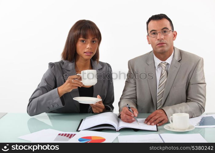 businessman and businesswoman examining a project and drinking coffee