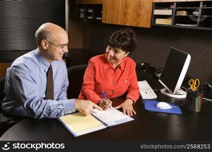 Businessman and businesswoman in office going over appointment calendar.