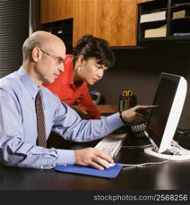 Businessman and businesswoman in office looking and pointing at computer monitor.