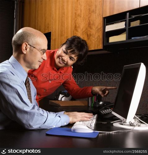 Businessman and businesswoman in office smiling looking and pointing at computer monitor.
