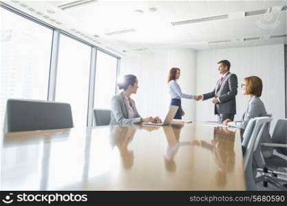 Businessman and businesswoman shaking hands in conference room