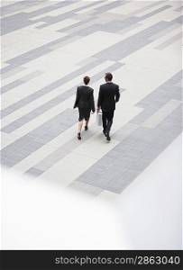 Businessman and businesswoman walking across outdoor plaza elevated view back view