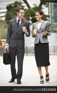 Businessman And Businesswoman Walking Along Street Holding Takeaway Coffee