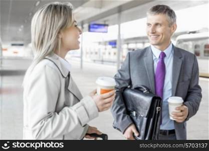 Businessman and businesswoman with coffee cups talking at railroad platform