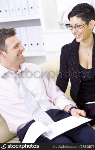 Businessman and businesswoman working together, stitting on sofa looking at financial figures, smiling.