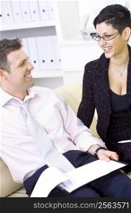 Businessman and businesswoman working together, stitting on sofa looking at financial figures, smiling.