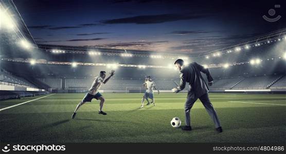 Businessman and player fighting for ball. Young businessman in suit playing football at stadium