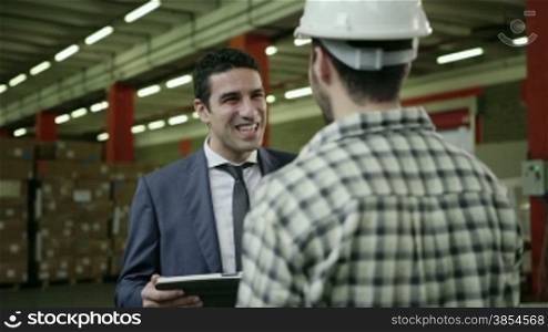 Businessman and supervisor in shipping facility talking to young man at work as manual worker, people working in warehouse, workers in industry. 3of19