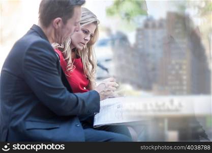Businessman and woman reading newspaper and chatting in city park
