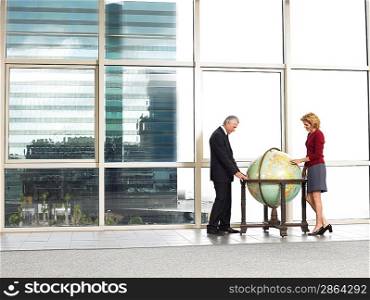 Businessman and woman studying large globe in office