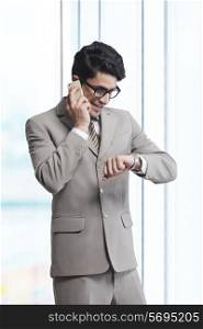 Businessman answering mobile phone while checking time in office