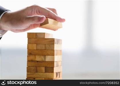 Businessman arranging wood block and stacking as tower by hand. Business organization and company growth progress. Success of strategy and money investment concept. Risk management project theme