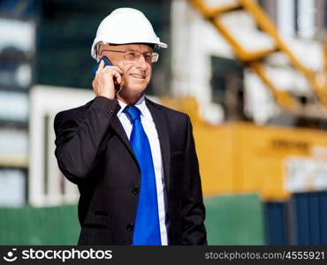 Businessman at construction site. Businesman wearing safety helmet with mobile phone at construction site