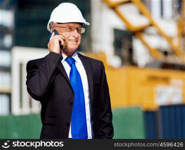 Businessman at construction site. Businesman wearing safety helmet with mobile phone at construction site