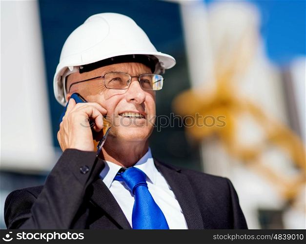 Businessman at construction site. Businesman wearing safety helmet with mobile phone at construction site