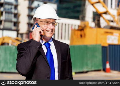 Businessman at construction site. Businesman wearing safety helmet with mobile phone at construction site