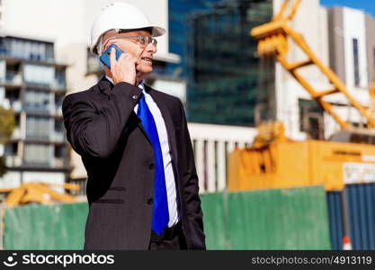 Businessman at construction site. Businesman wearing safety helmet with mobile phone at construction site