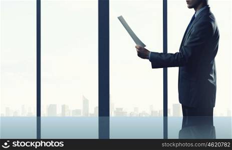 Businessman at work. Businessman standing against office window reading documents