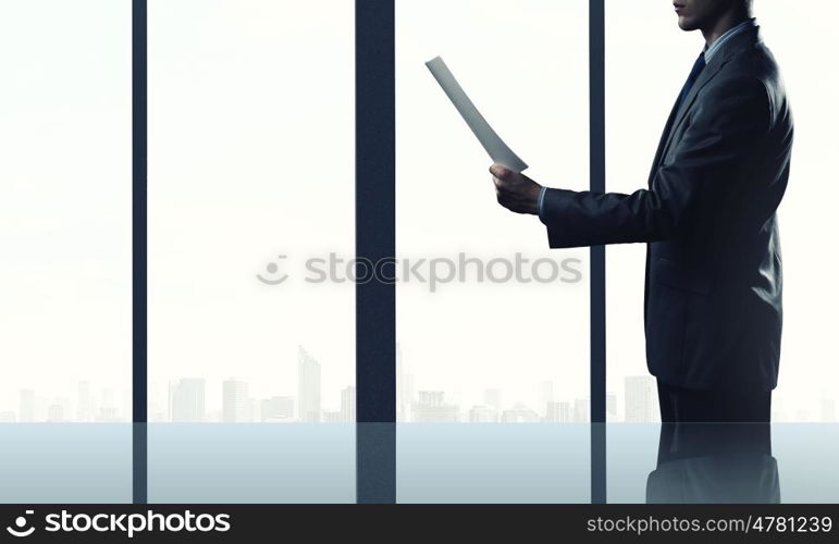 Businessman at work. Businessman standing against office window reading documents