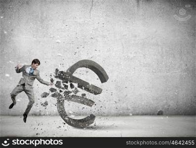 Businessman breaking stone euro symbol with karate punch. Financial crisis