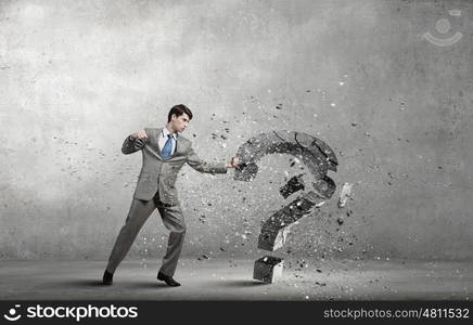 Businessman breaking stone question mark with karate kick. No more questions