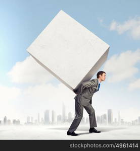 Businessman carrying cube. Image of businessman carrying big white cube on his back