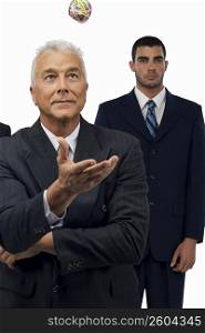 Businessman catching a rubber band ball with another businessman standing behind him