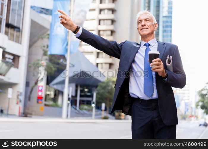 Businessman catching taxi in city. Businessman in suit catching taxi in city with cup of coffee in his hands