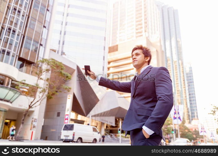 Businessman catching taxi in city. Businessman in suit catching taxi in city with mobile phone in his hands