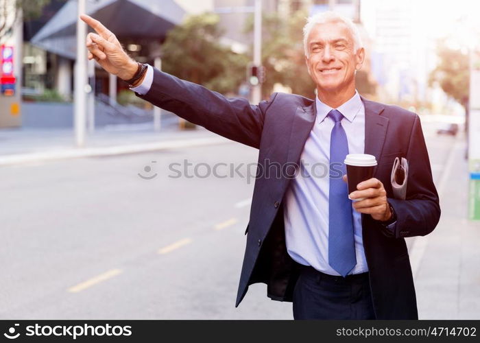 Businessman catching taxi in city. Businessman in suit catching taxi in city with cup of coffee in his hands