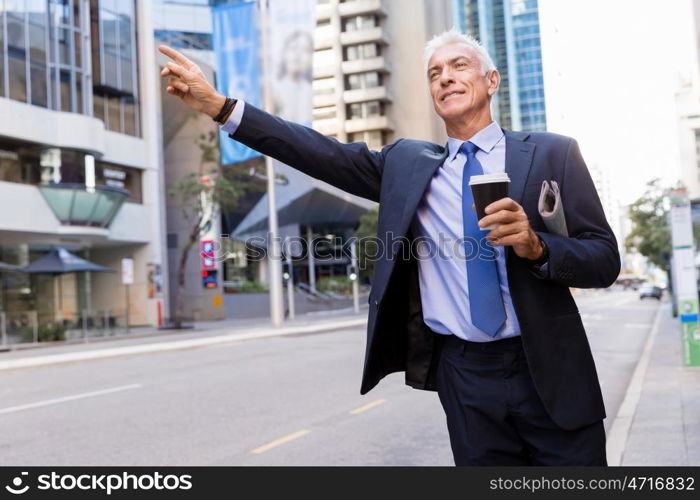 Businessman catching taxi in city. Businessman in suit catching taxi in city with cup of coffee in his hands