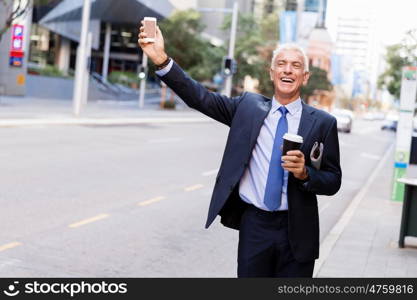 Businessman catching taxi in city. Businessman in suit catching taxi in city with cup of coffee in his hands