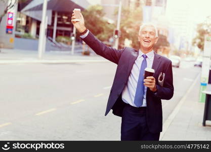 Businessman catching taxi in city. Businessman in suit catching taxi in city with cup of coffee in his hands