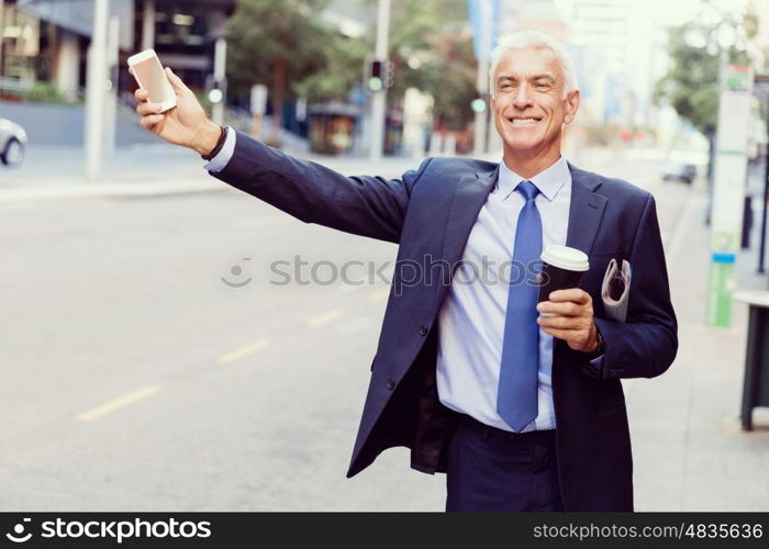 Businessman catching taxi in city. Businessman in suit catching taxi in city with cup of coffee in his hands