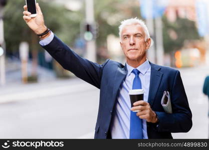 Businessman catching taxi in city. Businessman in suit catching taxi in city with cup of coffee in his hands