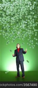 businessman catchs flying banknotes on green background