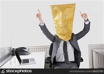 Businessman cheering with smiley drawn on paper bag over face in office
