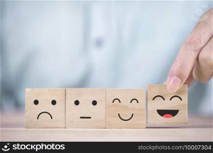 Businessman chooses a smiley face happy symbol on wooden block , Services and Customer satisfaction survey concept