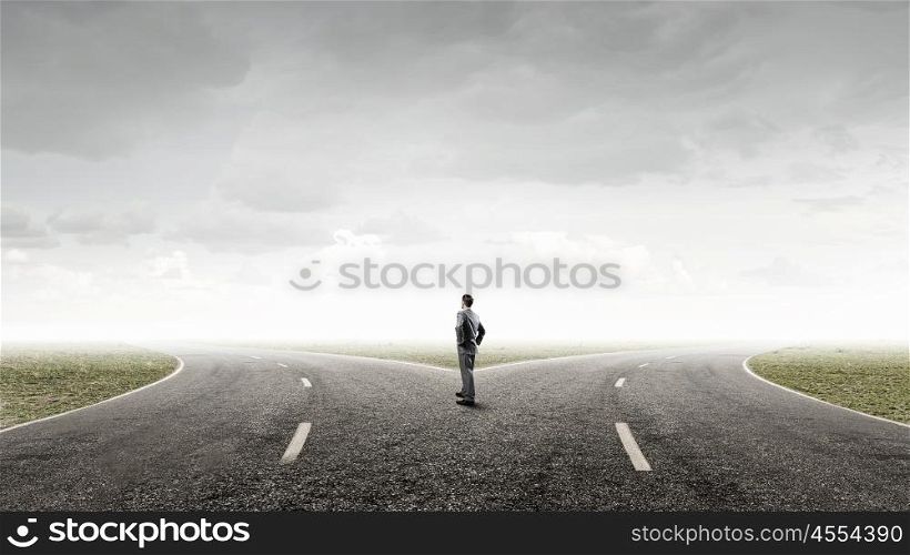 Businessman choosing his way. Young businessman with arms on waist standing on asphalt road