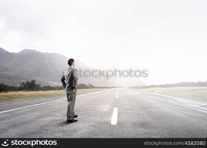 Businessman choosing his way. Young businessman with arms on waist standing on asphalt road