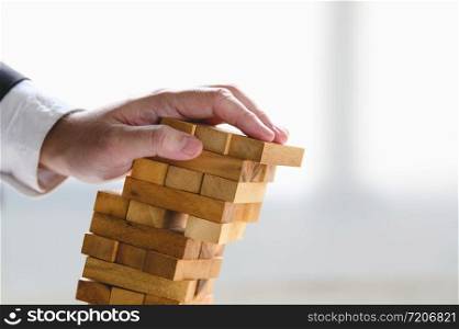 Businessman collapsing stacked tower wood block by hand as failure or bankrupt project. Business organization and company unsuccessful progress. Strategy and money investment. Risk management