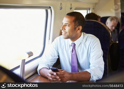 Businessman Commuting To Work On Train Using Mobile Phone