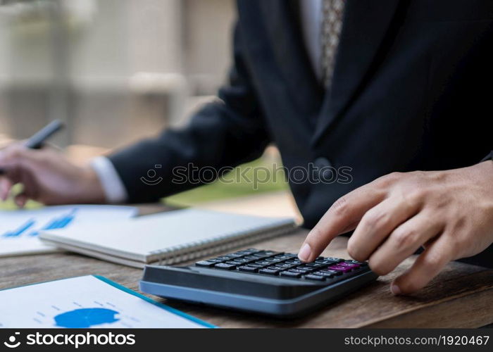 Businessman concept the male accountant using the calculator to check the correctness of the numerical data in the info chart on the wooden table.